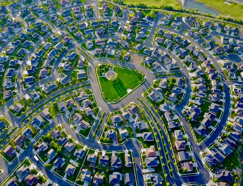 Completed homes and curved streets surrounding a central park, with golf fairways beyond